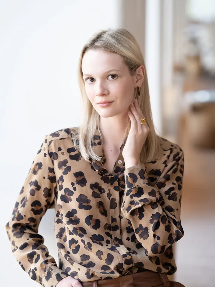 blonde woman sitting down touching next wearing an animal print blouse and brown leather pants