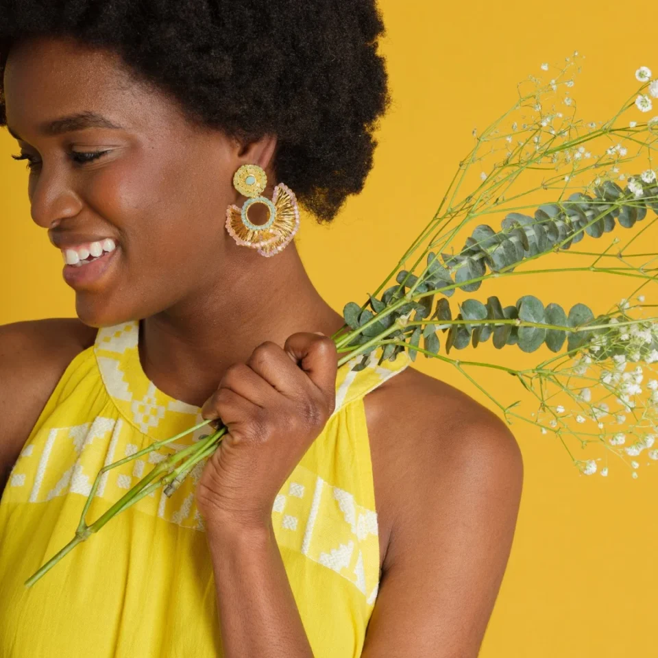 close up of young black model smiling wearing summer yellow dress holding wildflowers