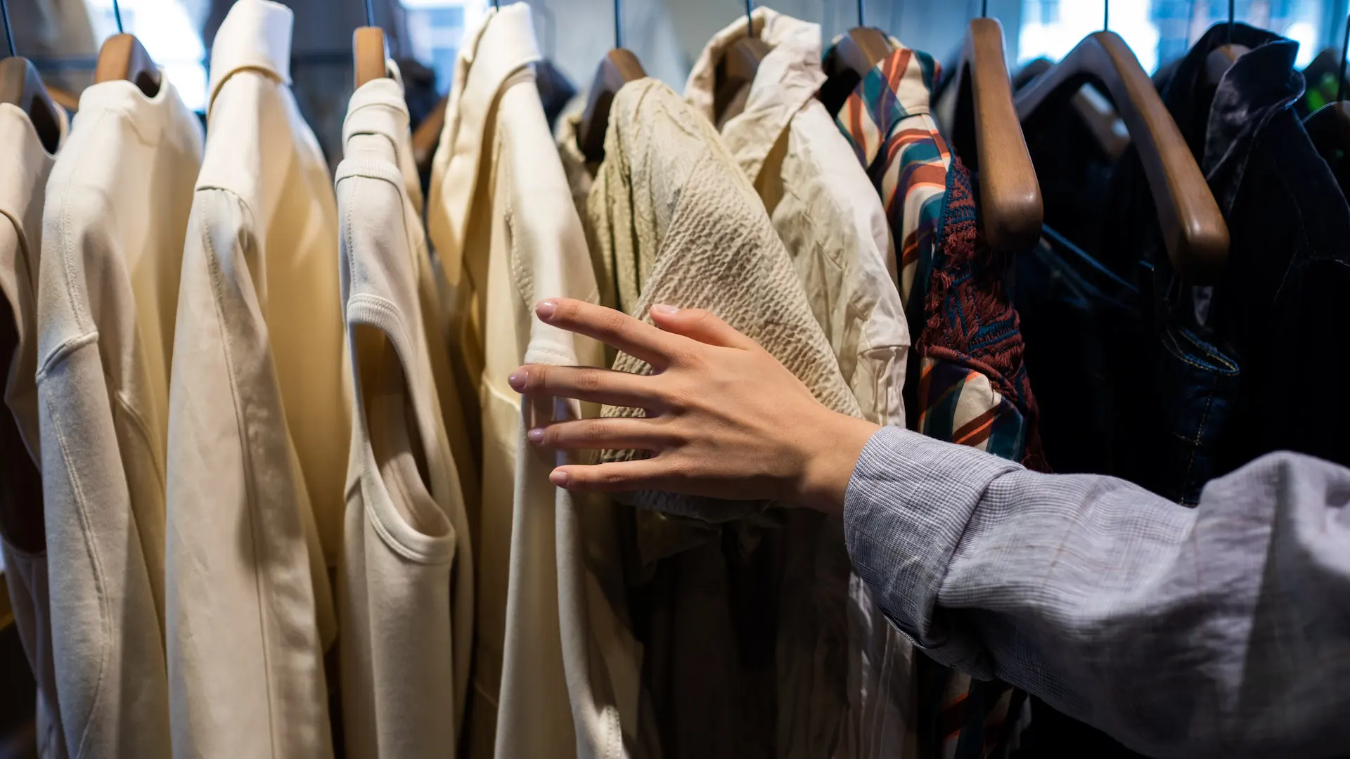 Close up of woman's hands flipping through shirts on a clothes rack
