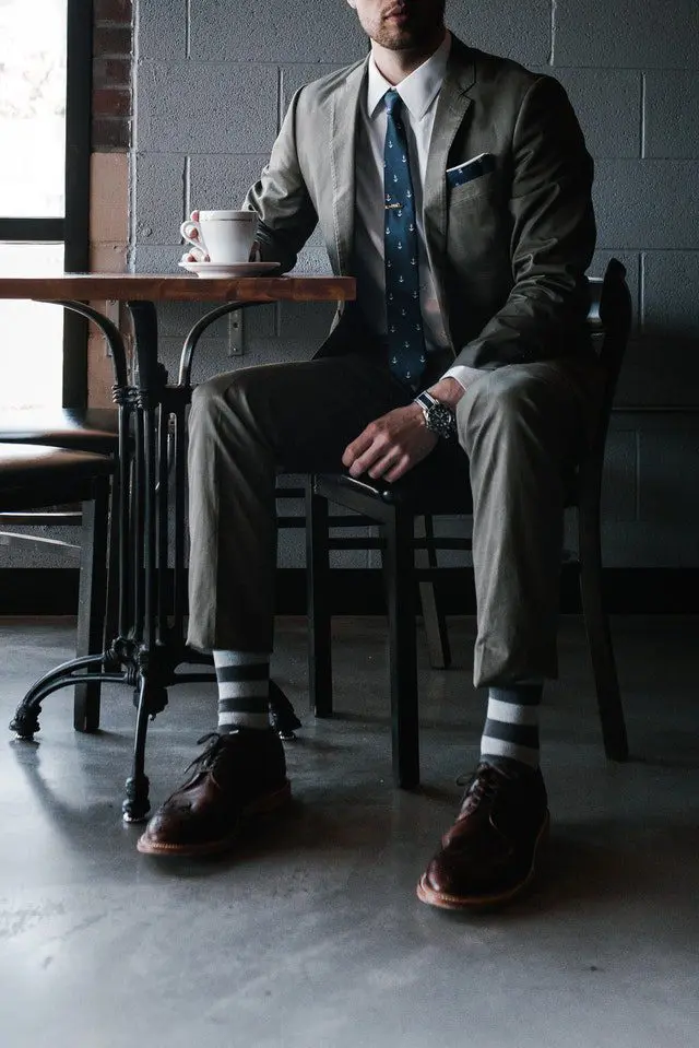man wearing dark grey suit sitting down in a cafe shop