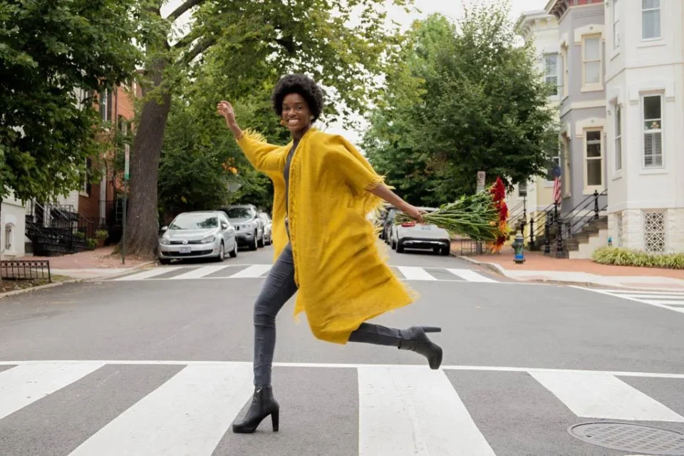 young black model running throught an crosswalk and laughing wearing a mustard cardigan and jeans