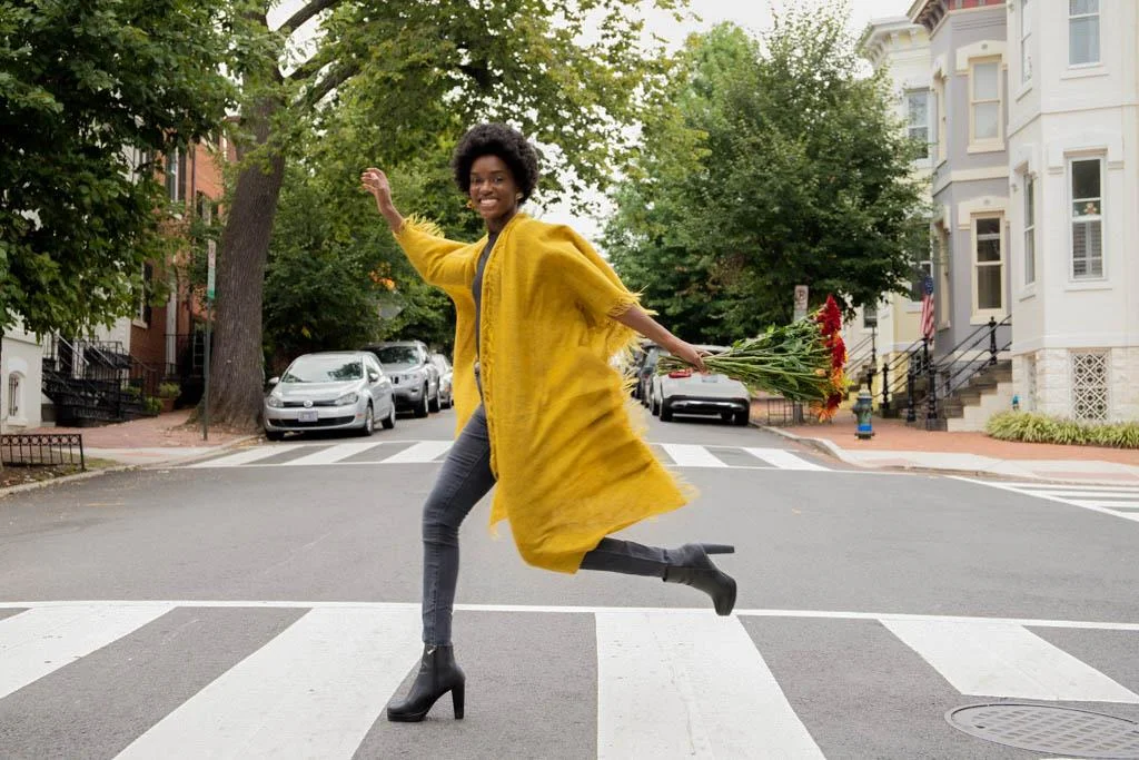 young black model running throught an crosswalk and laughing wearing a mustard cardigan and jeans