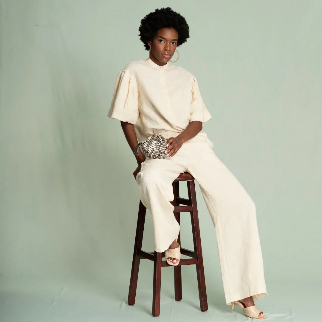 young black woman with a stylish afro wearing cream colored fashion jumpsuit sitting on stool holding her bag